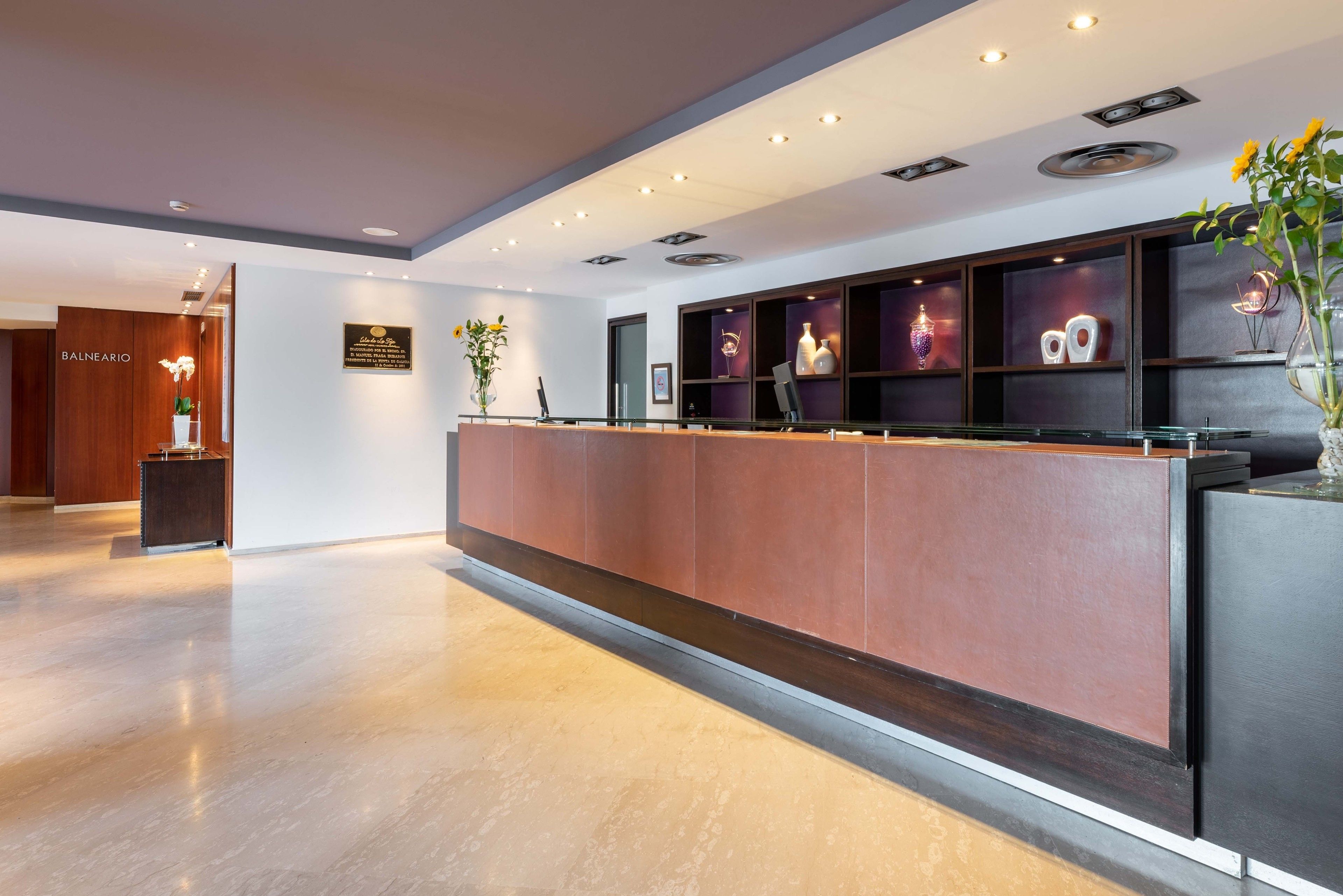 Un área de recepción con un mostrador de madera, un letrero que indica Balneario y una pared decorada con objetos y un jarrón con flores.