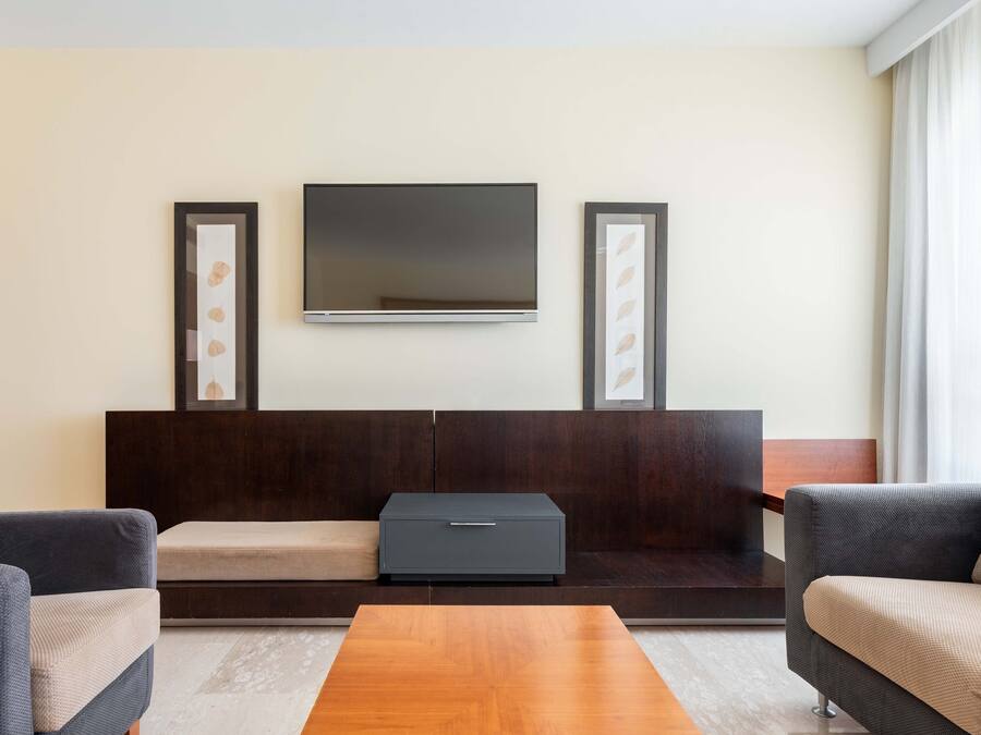 Un salon moderne avec un téléviseur à écran plat fixé au mur, un canapé en bois foncé, un canapé beige et une table basse en bois.