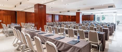 Un salón de conferencias con filas de mesas y sillas, equipado con botellas de agua y tarjetas de identificación.