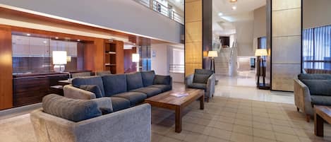 A modern lobby with a high ceiling, a staircase, and a seating area with sofas and armchairs.