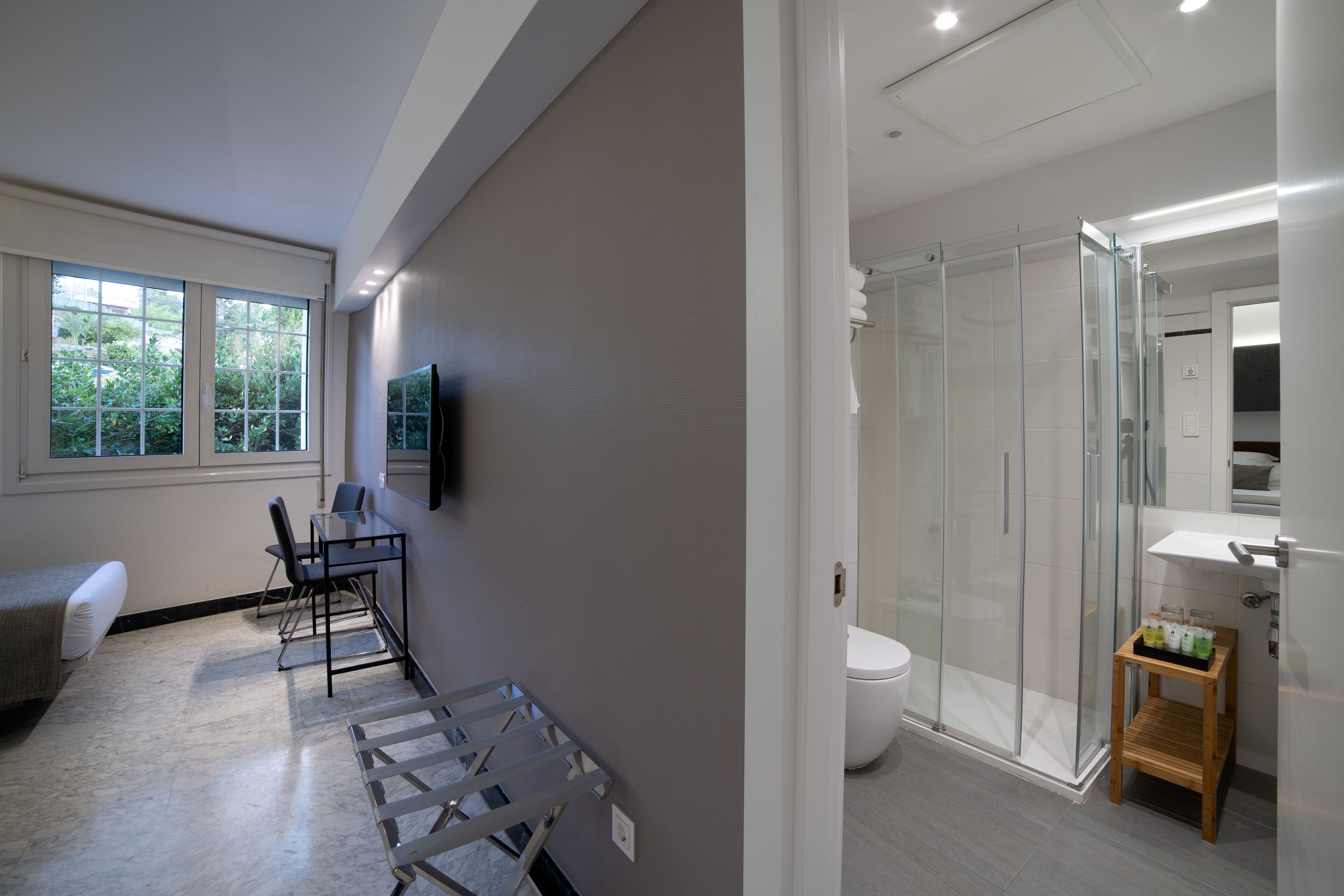 A modern bathroom with a glass shower enclosure, a toilet, and a small wooden shelf with toiletries.