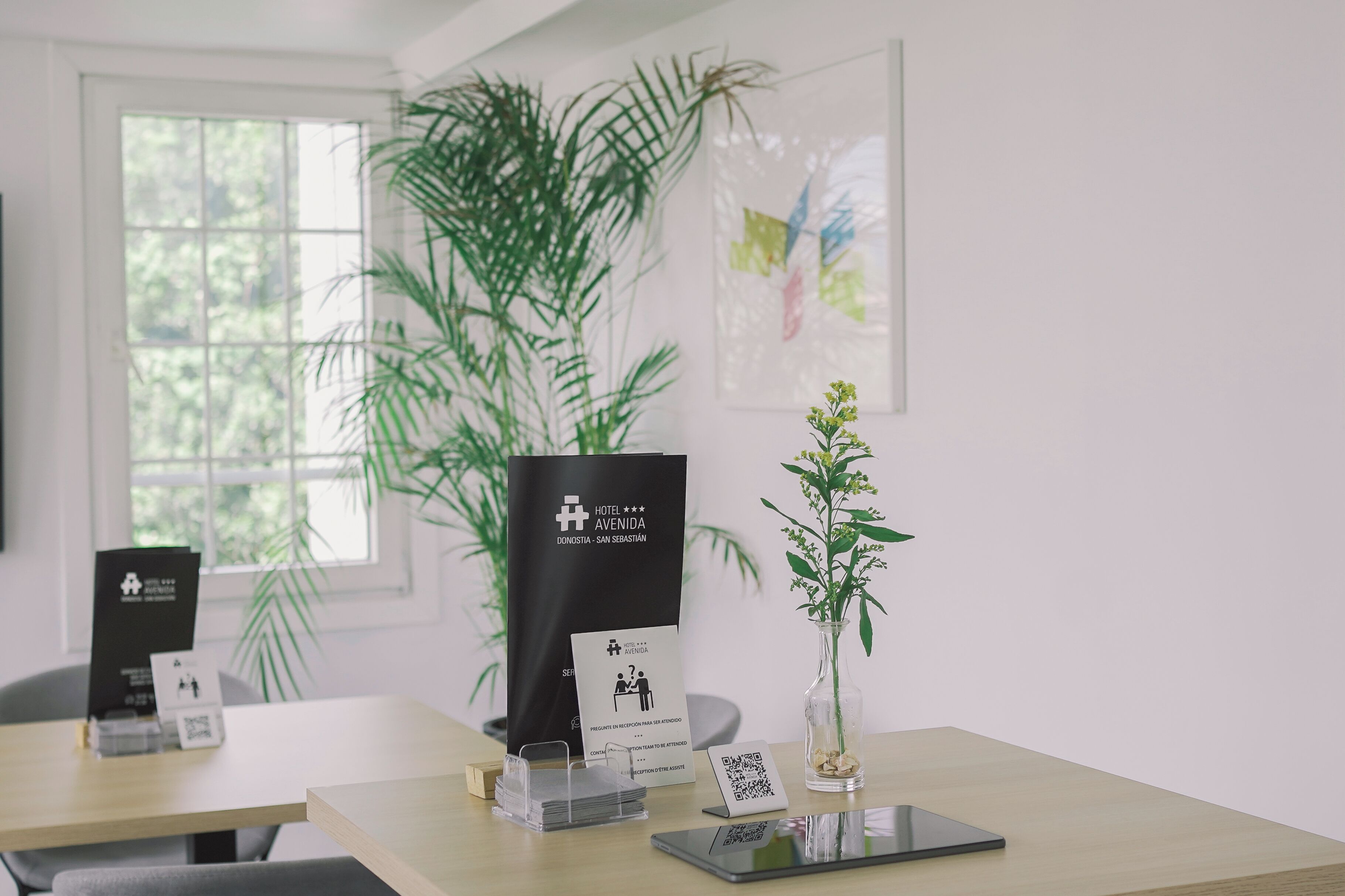 Un comptoir d’accueil d’hôtel avec des brochures d’information, un code QR et une petite plante en pot.