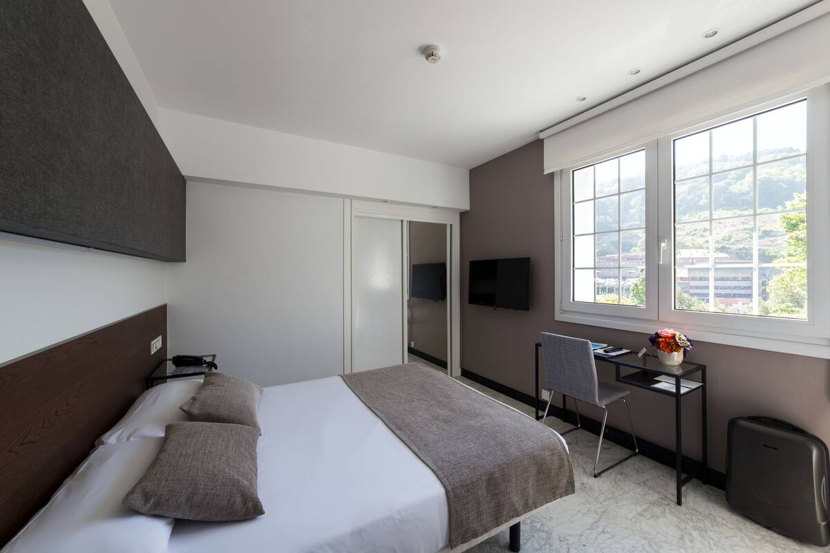 A modern hotel room with a bed, a desk, and a TV.