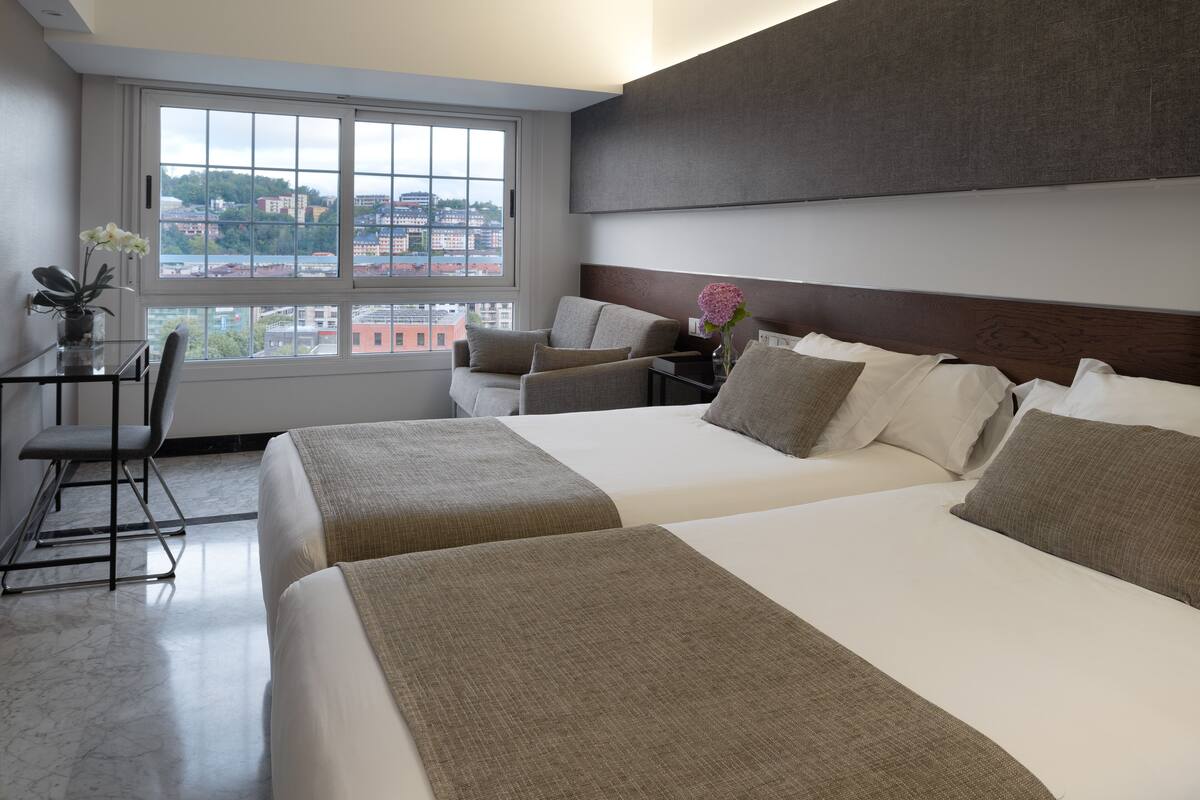 A hotel room with two beds, a desk, and a chair.