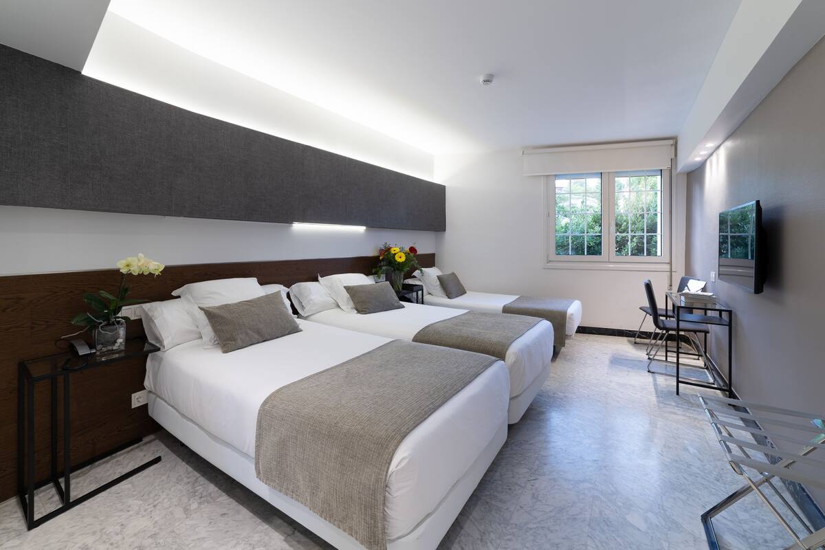 A modern hotel room with two beds, a desk, and a TV.