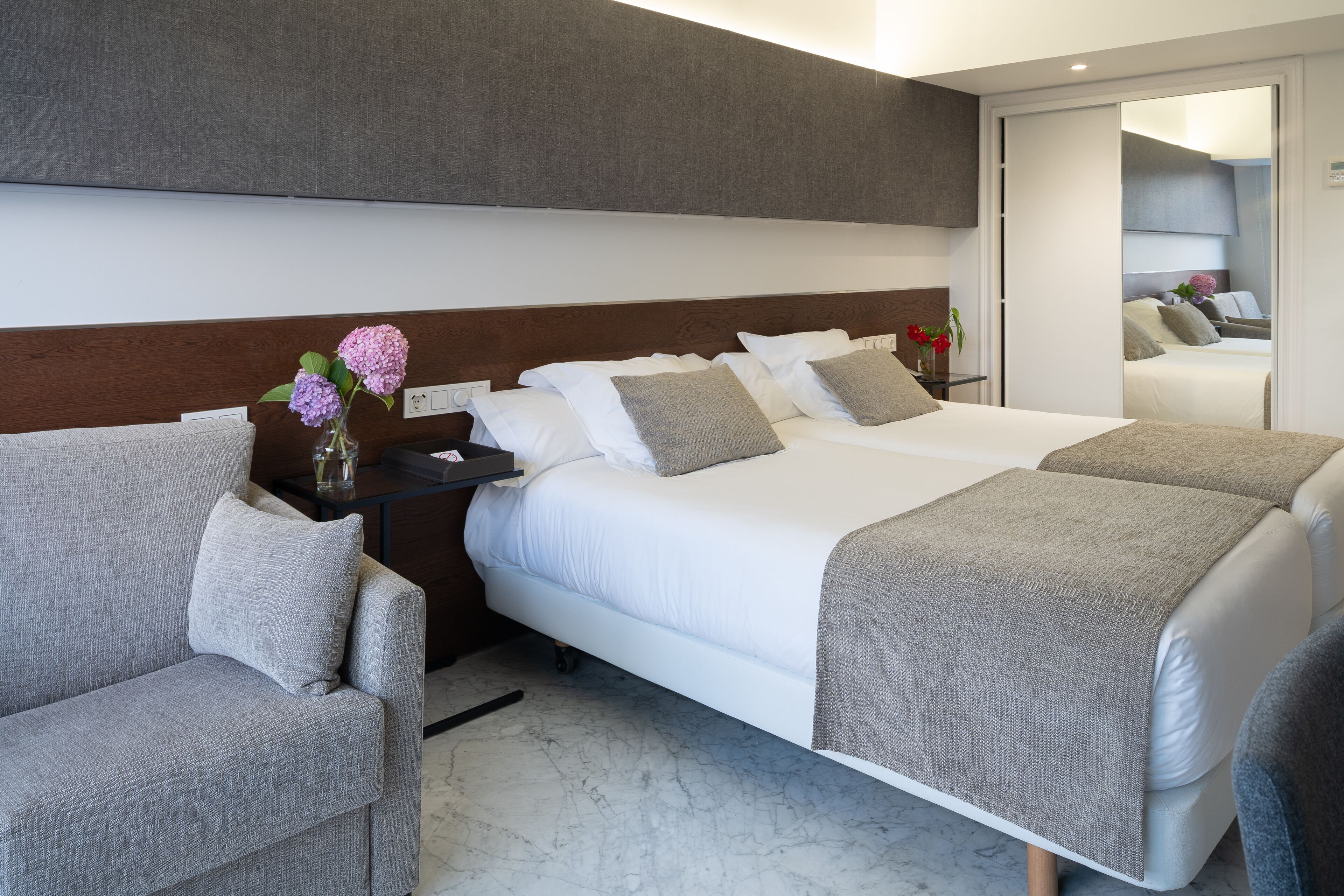 Una habitación de hotel moderna con una cama grande, dos mesitas de noche y un sofá.