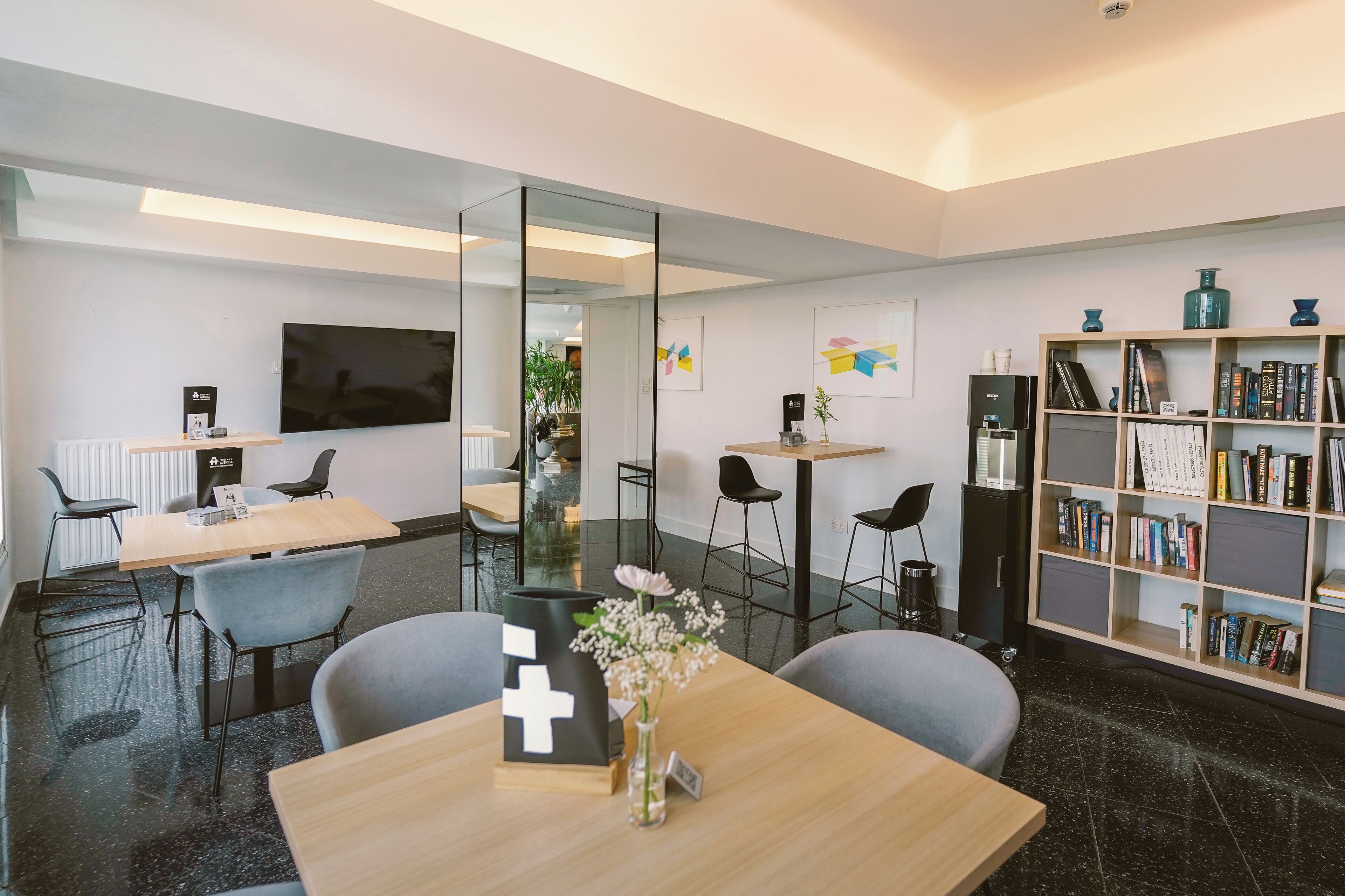 Een moderne kantoorruimte met een houten tafel, stoelen, een boekenkast en een grote flatscreen-televisie.