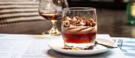 A dessert glass with whipped cream and nuts on a plate, a wine glass, and a menu on a table.