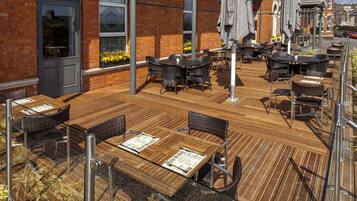 An outdoor patio with wooden tables and chairs, brick walls, and umbrellas.