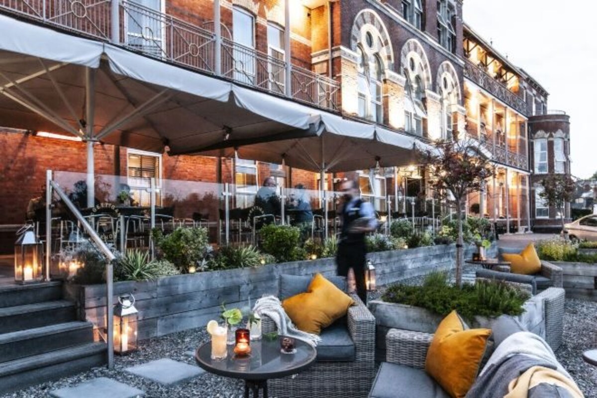 An outdoor seating area with tables and chairs, a covered patio, and a building with a brick facade.