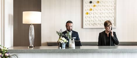 A reception desk with a modern chandelier, a wall-mounted art piece, and a check-in counter.