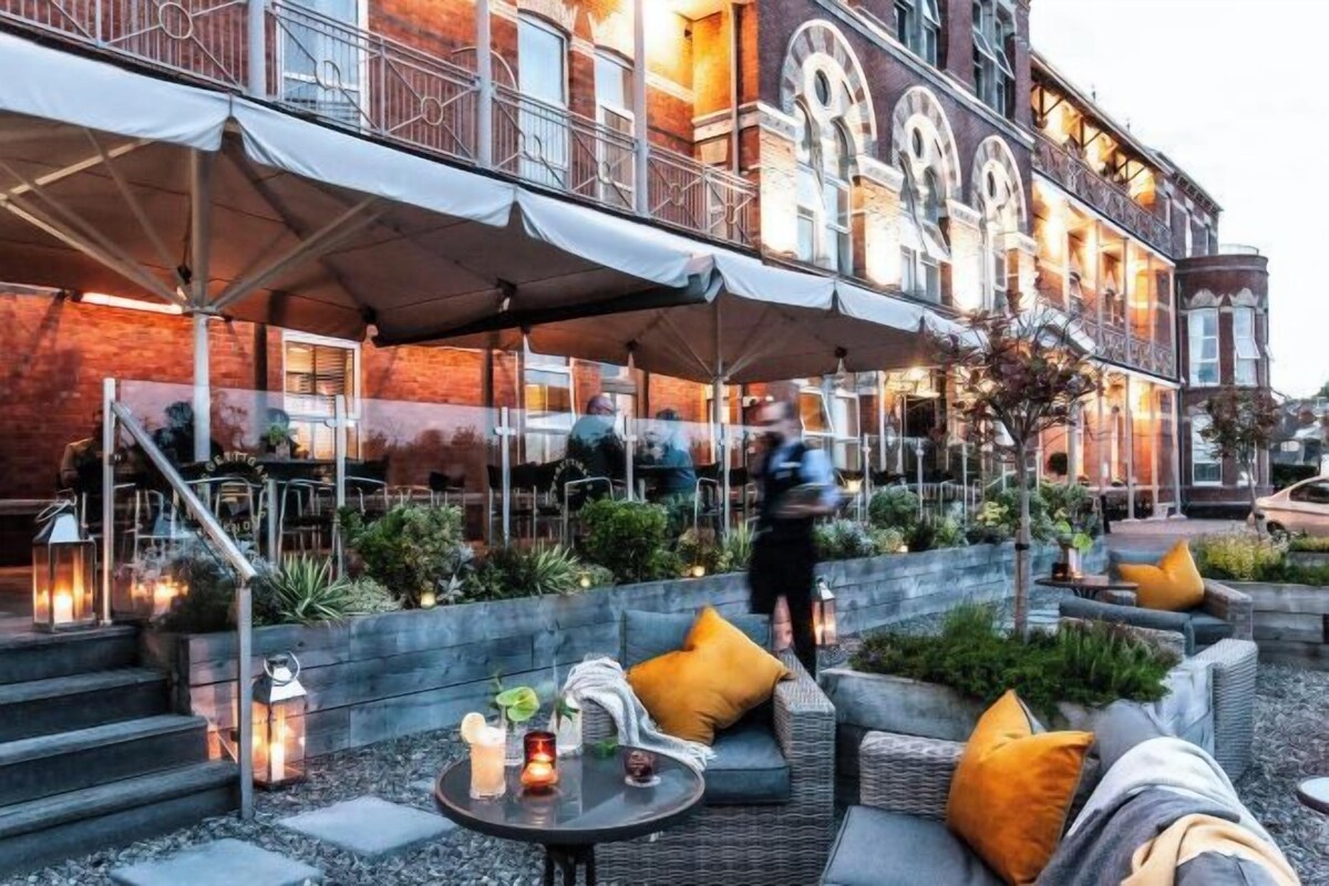 An outdoor seating area with tables and chairs, a covered walkway, and a building with a red facade.