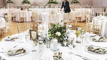 A formal dining setup with round tables, white tablecloths, and gold cutlery.