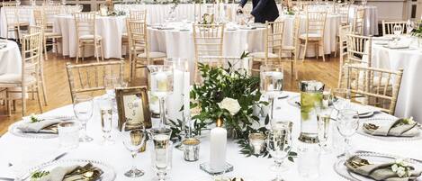 Une salle à manger aménagée de façon élégante, avec des tables rondes, des nappes blanches et des couverts dorés.
