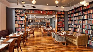 A library with bookshelves, tables, chairs, and a bar area. - The Address Cork (Cork)