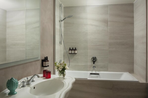Une salle de bain avec un lavabo, un miroir, une douche et un vase de fleurs.