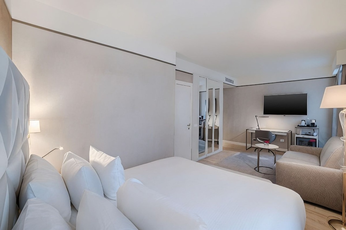 A hotel room with a bed, a desk, a chair, a television, and a wardrobe.