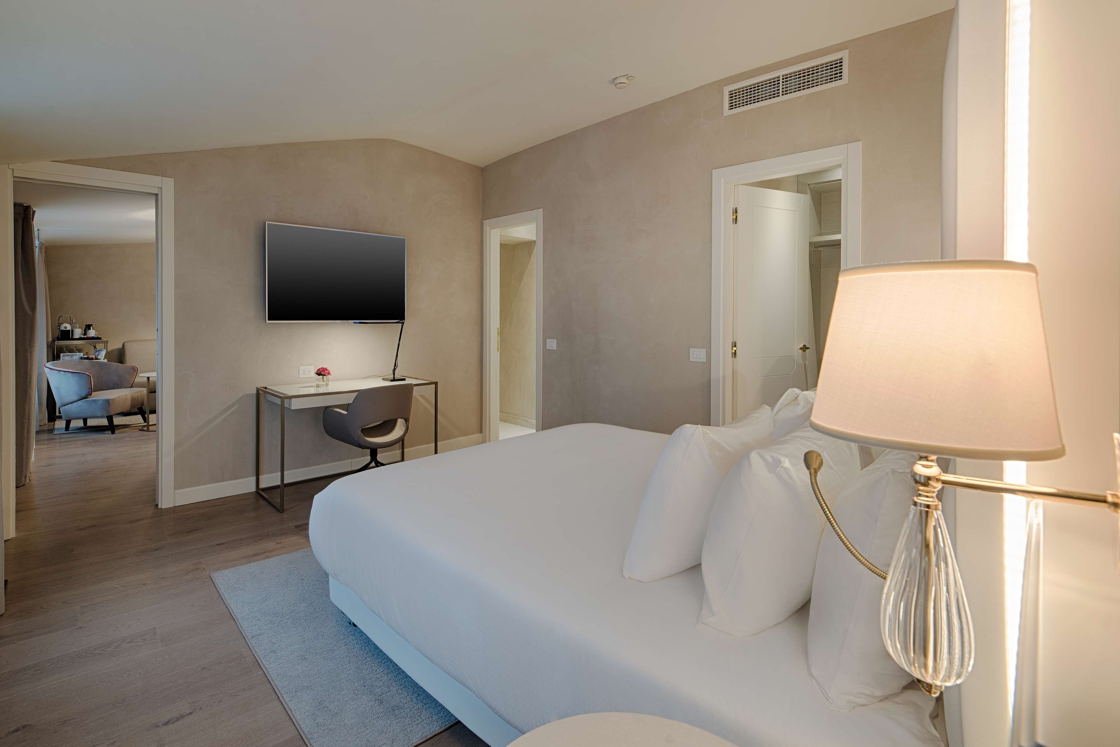 Une chambre d’hôtel avec un grand lit, un bureau avec une chaise, un téléviseur fixé au mur et une lampe.