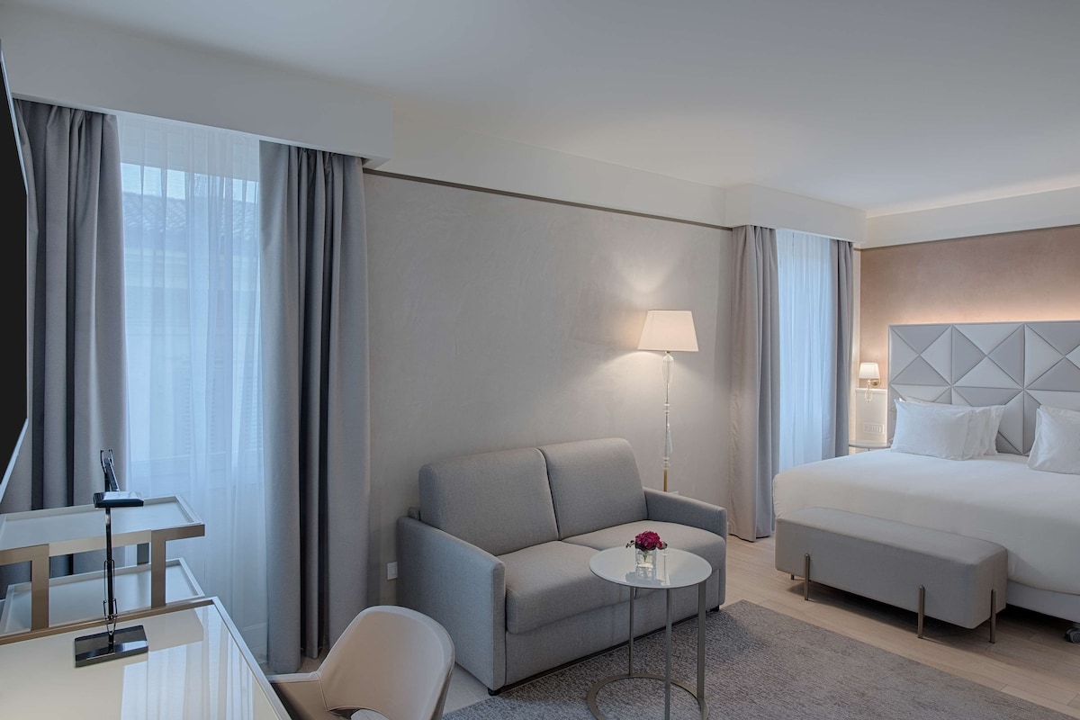 A hotel room with a bed, a sofa, a small table, a desk, and a chair.