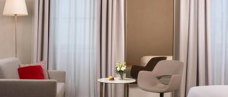 A hotel room with a sofa, a chair, a small table with a vase of flowers, and a lamp.