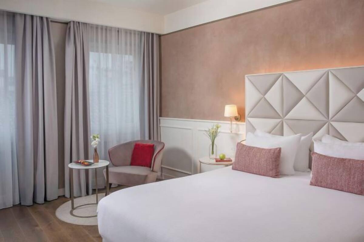 Une chambre d’hôtel avec un grand lit, une chaise, une petite table et une table de chevet avec une lampe.