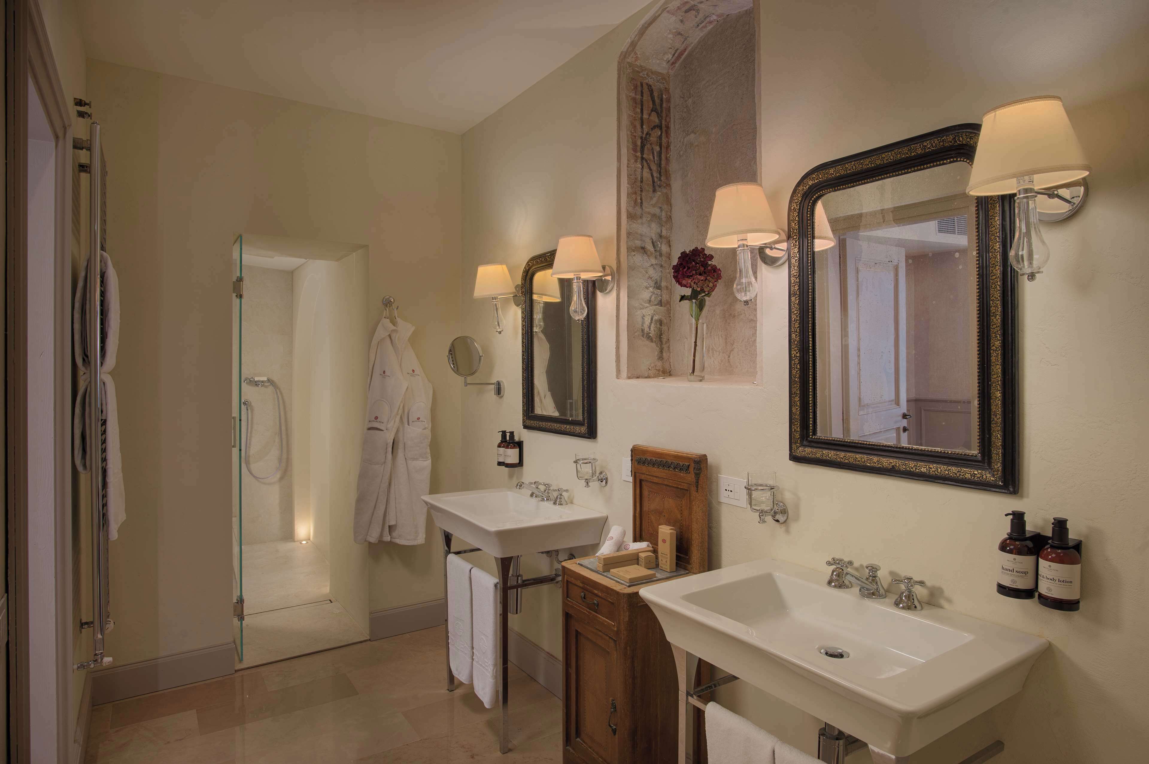 A bathroom with two sinks, a shower, and a mirror with wall sconces.