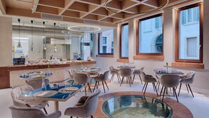 A modern dining area with round tables, grey upholstered chairs, and a central glass table. - NH Collection Palazzo Verona (Verona)