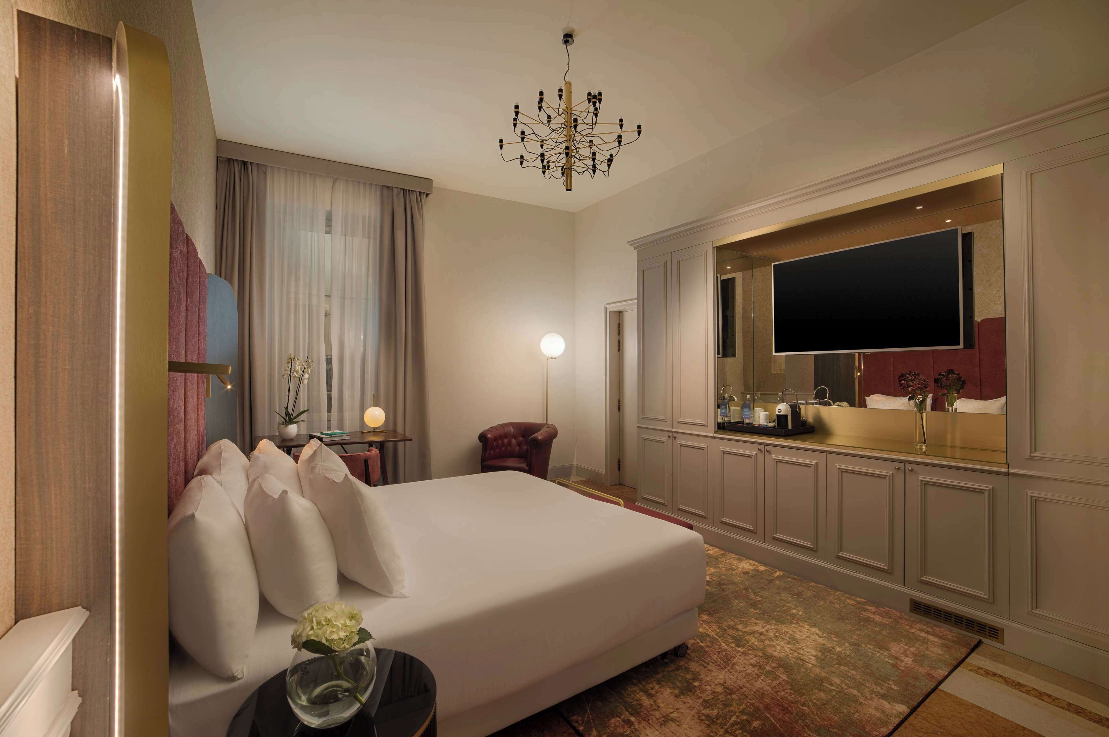 Une chambre d’hôtel dotée d’un grand lit, d’un téléviseur à écran plat, d’un lustre, d’un bureau avec une lampe et d’un miroir.