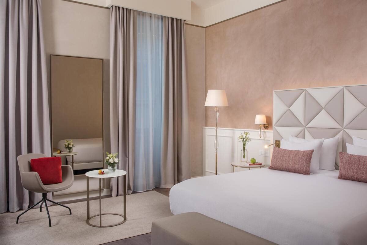 Une chambre d’hôtel avec un lit, une chaise, une petite table, une lampe et un miroir.