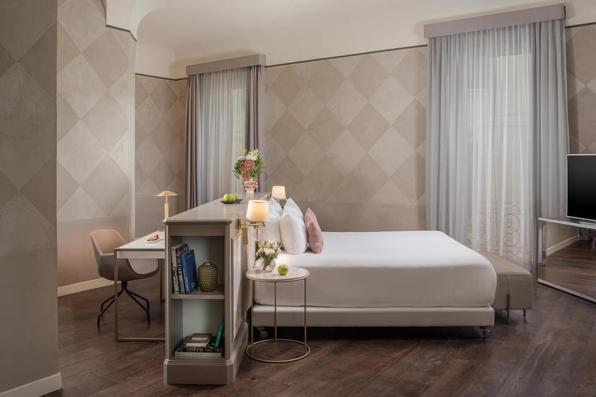 Une chambre d’hôtel moderne équipée d’un lit, d’un bureau, d’une chaise, d’une petite table avec une lampe et d’un téléviseur.