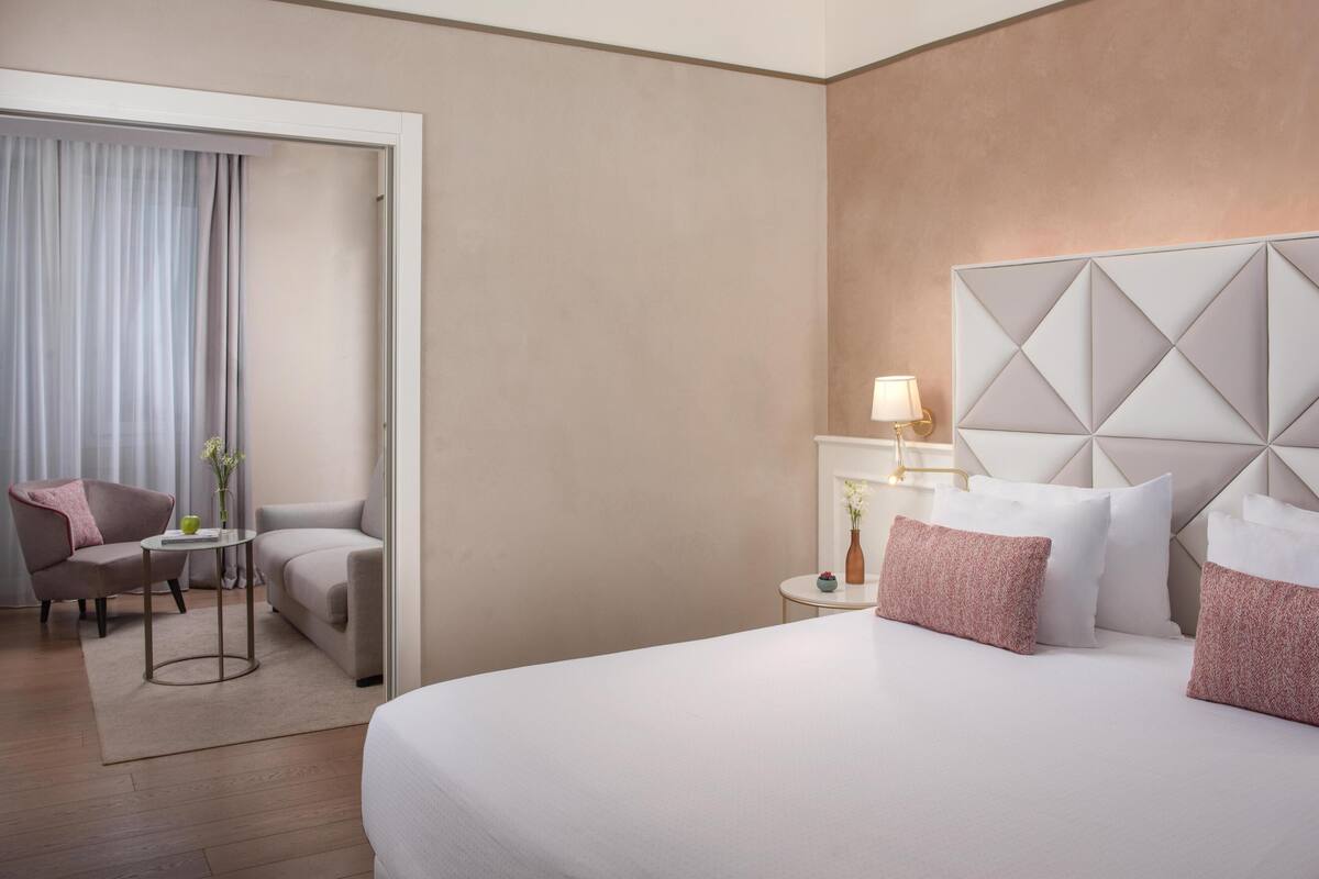 Une chambre d’hôtel comprenant un lit, une chaise, une petite table, une lampe et un panneau décoratif mural.