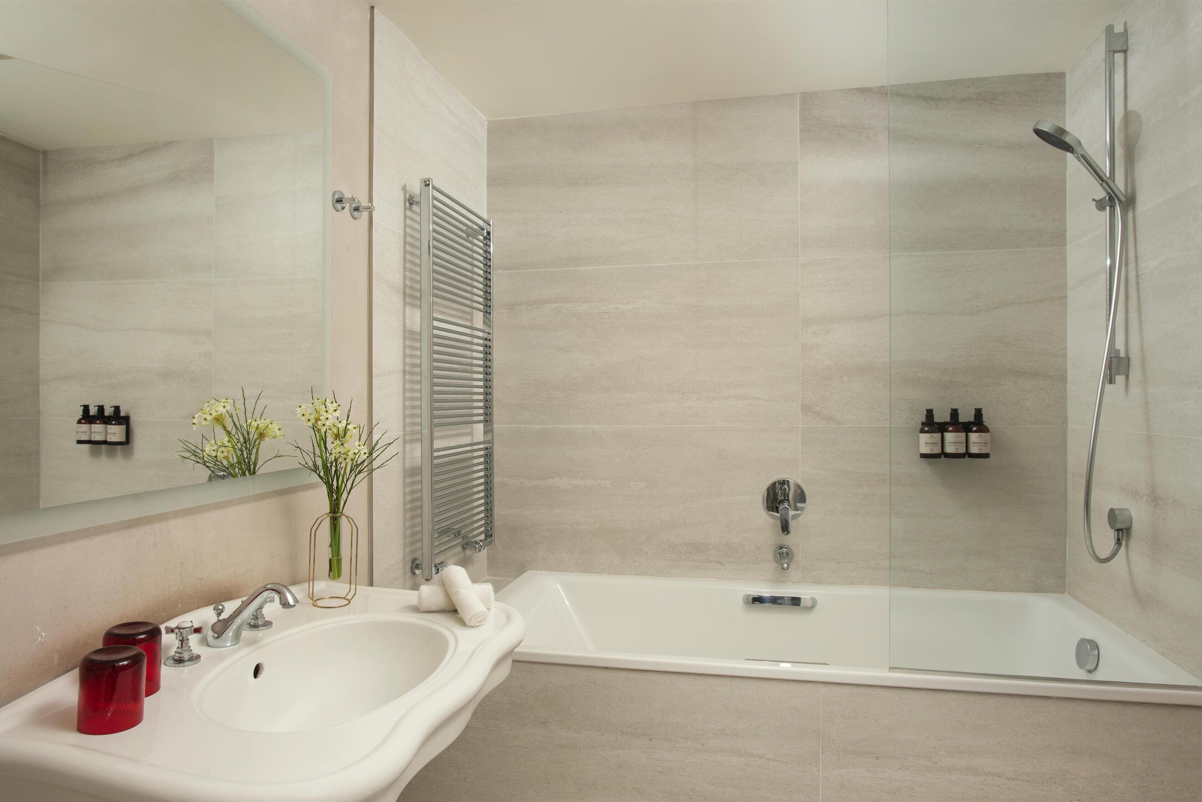 A bathroom with a sink, mirror, shower, and toiletries.
