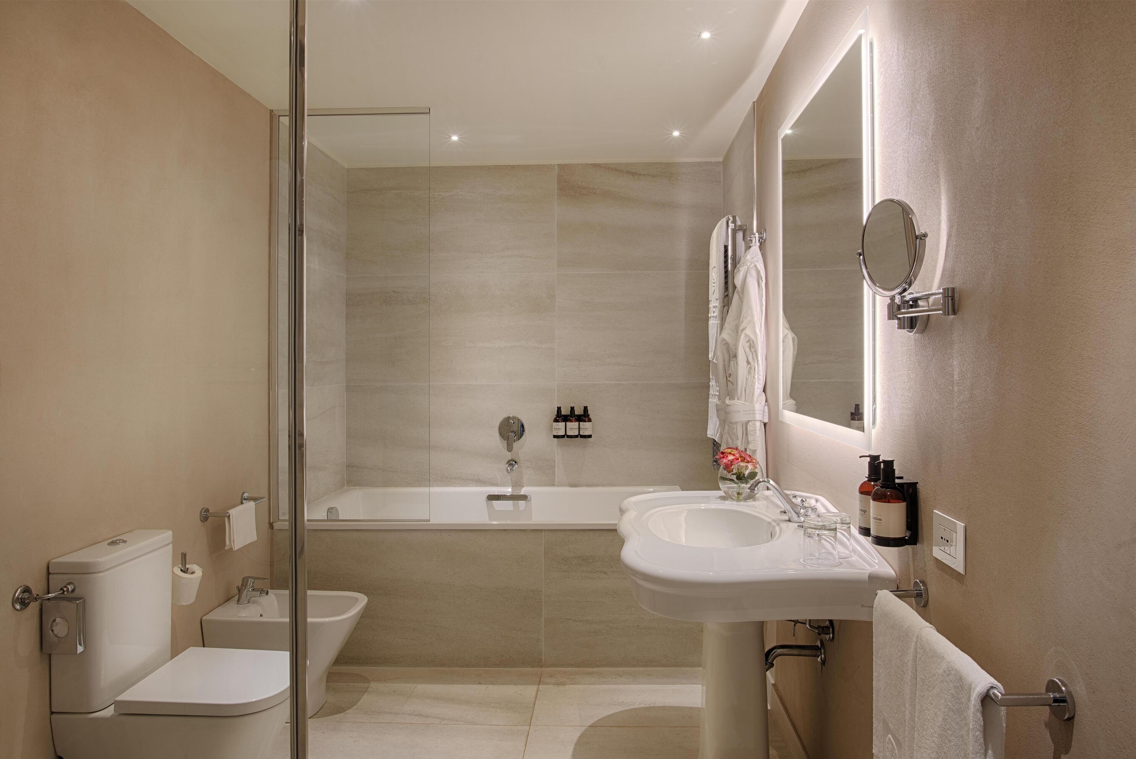 A modern bathroom with a toilet, bidet, bathtub, and a sink with a mirror.