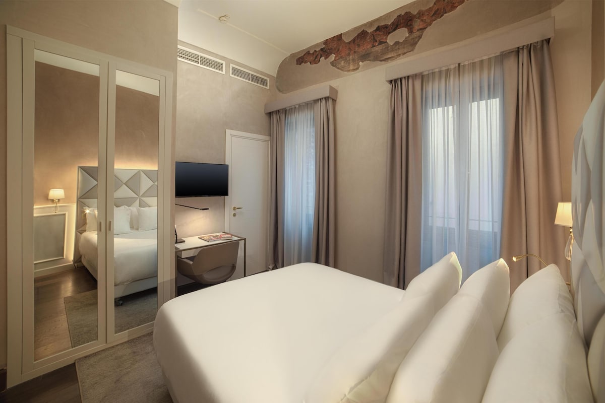 Une chambre d’hôtel avec un grand lit, une télévision, un bureau avec une lampe et une armoire.