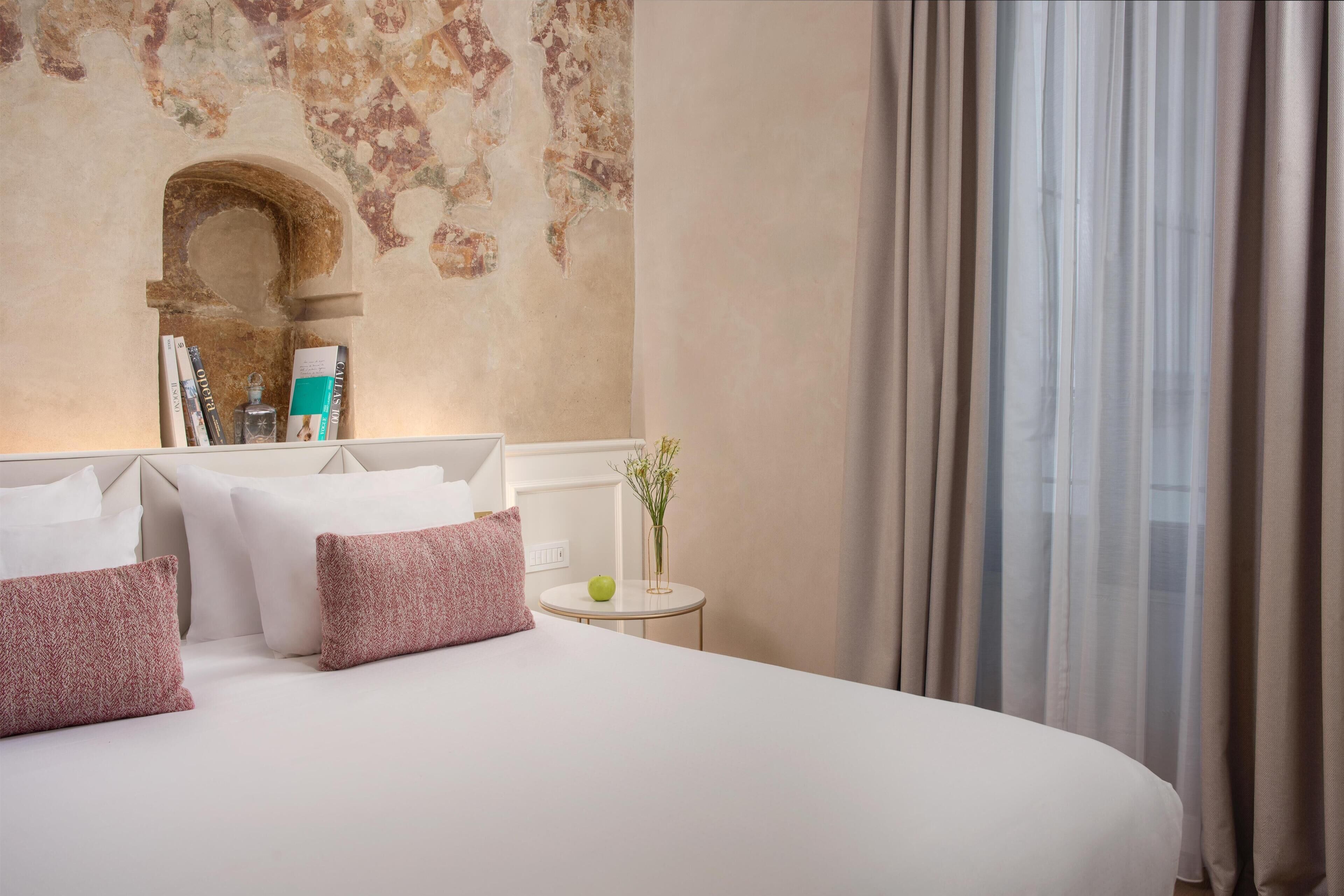 A neatly made bed with pillows, a small bedside table with a vase and a book, and a wall with a decorative arch.