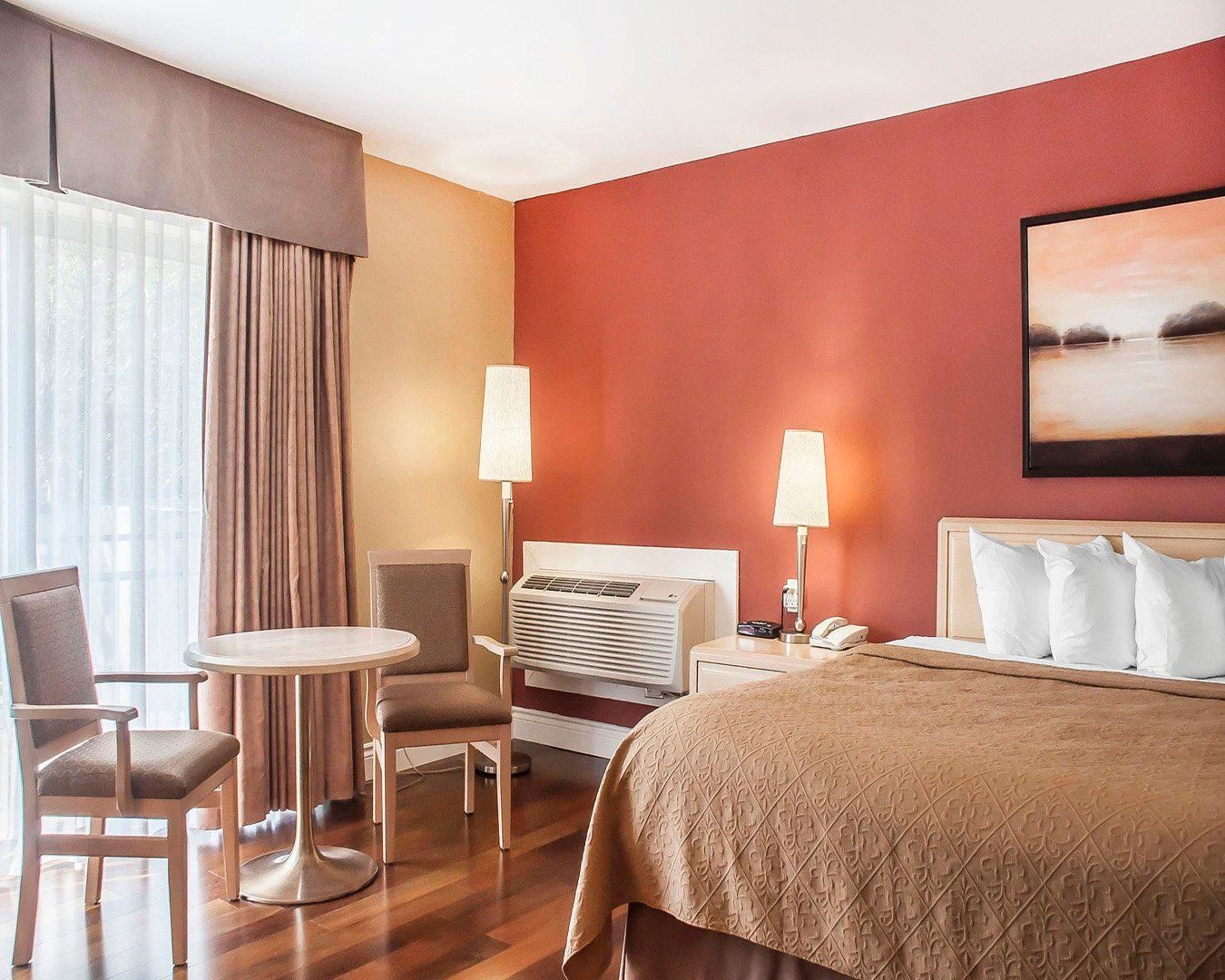 A hotel room with a bed, a desk, a chair, a lamp, and a painting on the wall.