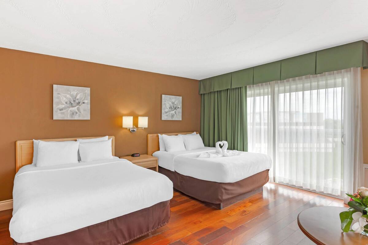 A hotel room with two beds, a round table, and a large window with sheer curtains.