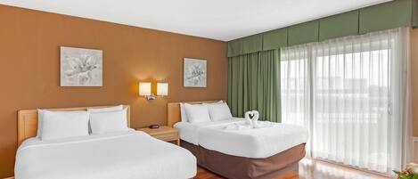 A hotel room with two beds, a round table, and a large window with sheer curtains.