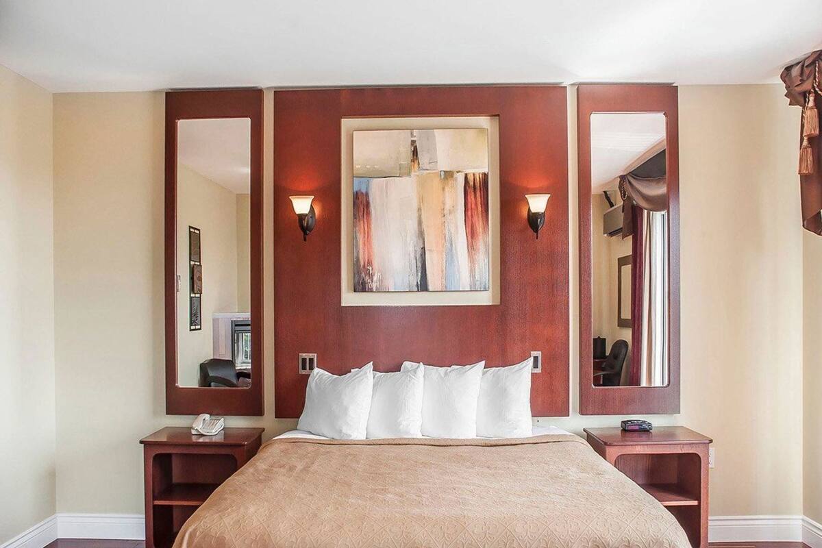 A hotel room with a large bed, two bedside tables, a painting on the wall, and two wall-mounted lamps.