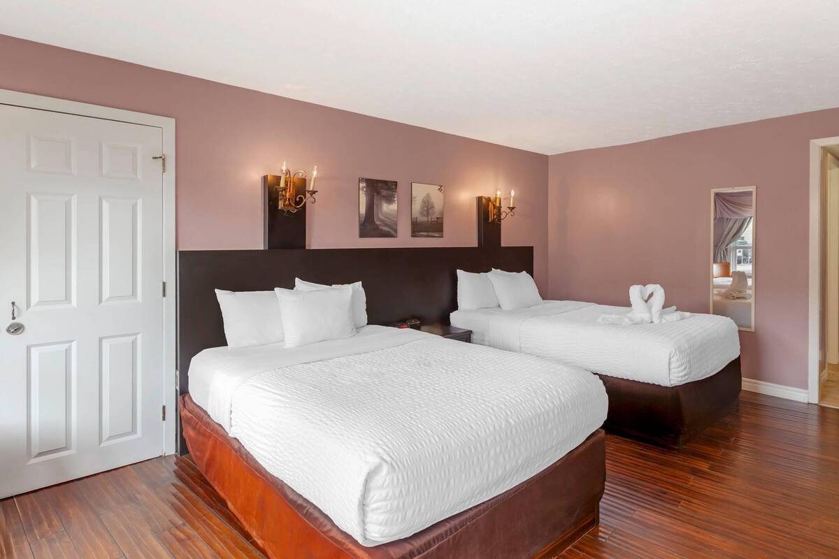 A hotel room with two beds, a white door, and wall-mounted sconces.