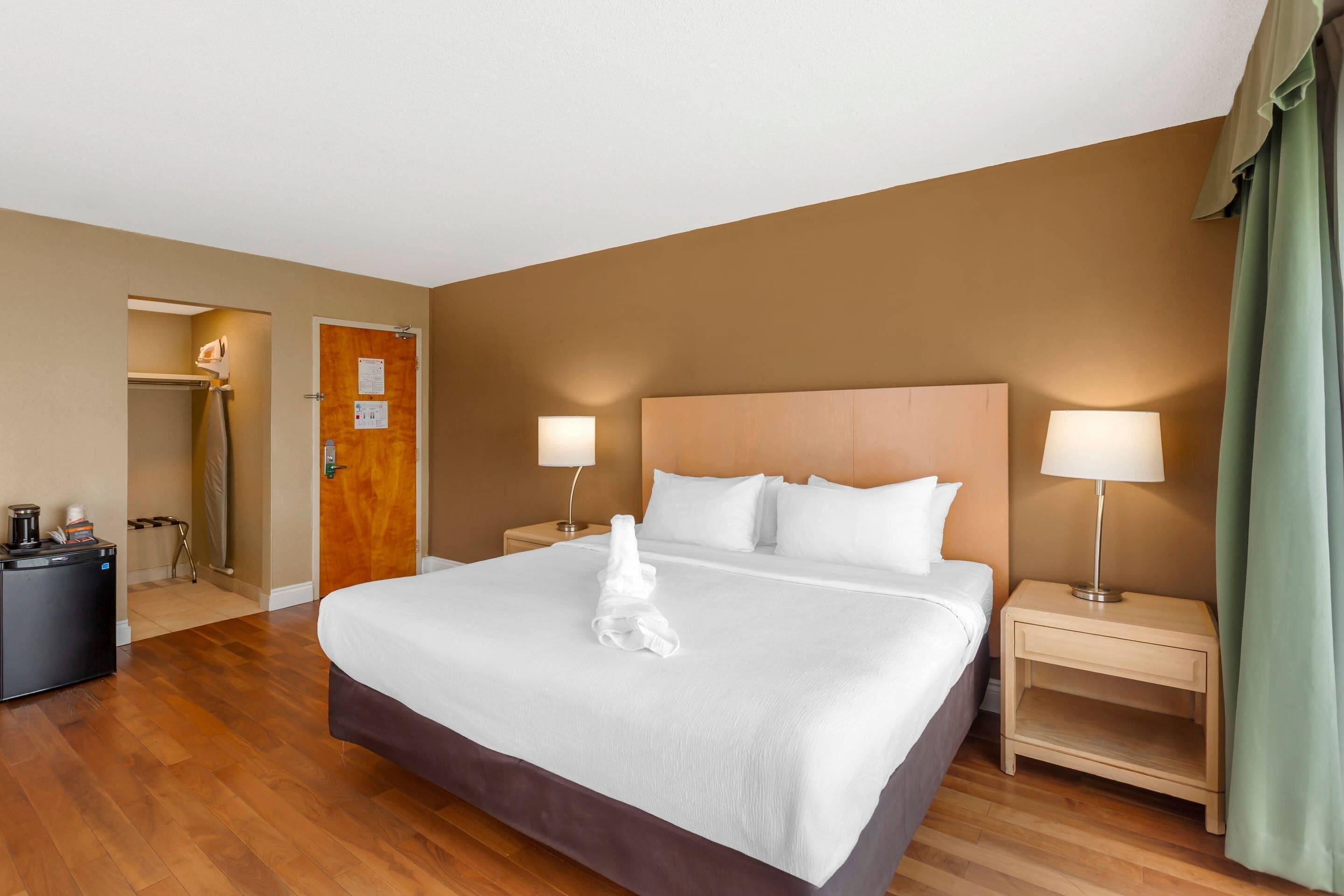 Habitación de hotel con una cama grande, dos mesitas de noche con lámparas, una puerta de madera y un escritorio pequeño con lámpara.