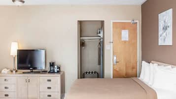 A hotel room with a bed, a television, a desk with a lamp, a shower, and a door with a sign.