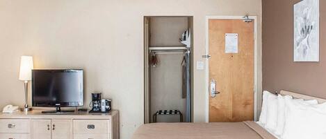 A hotel room with a bed, a television, a desk with a lamp, a shower, and a door with a sign.