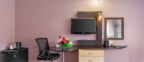 Quarto de hotel compacto com escrivaninha, cadeira e um pequeno frigorífico.