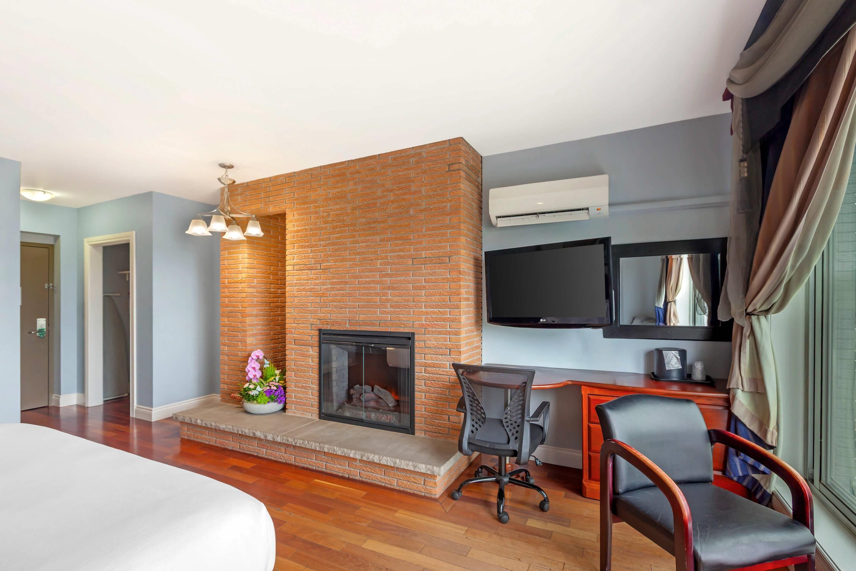 Une chambre d’hôtel dotée d’une cheminée en briques, d’un téléviseur à écran plat fixé au mur, d’un bureau en bois, d’un fauteuil confortable et d’un grand lit.