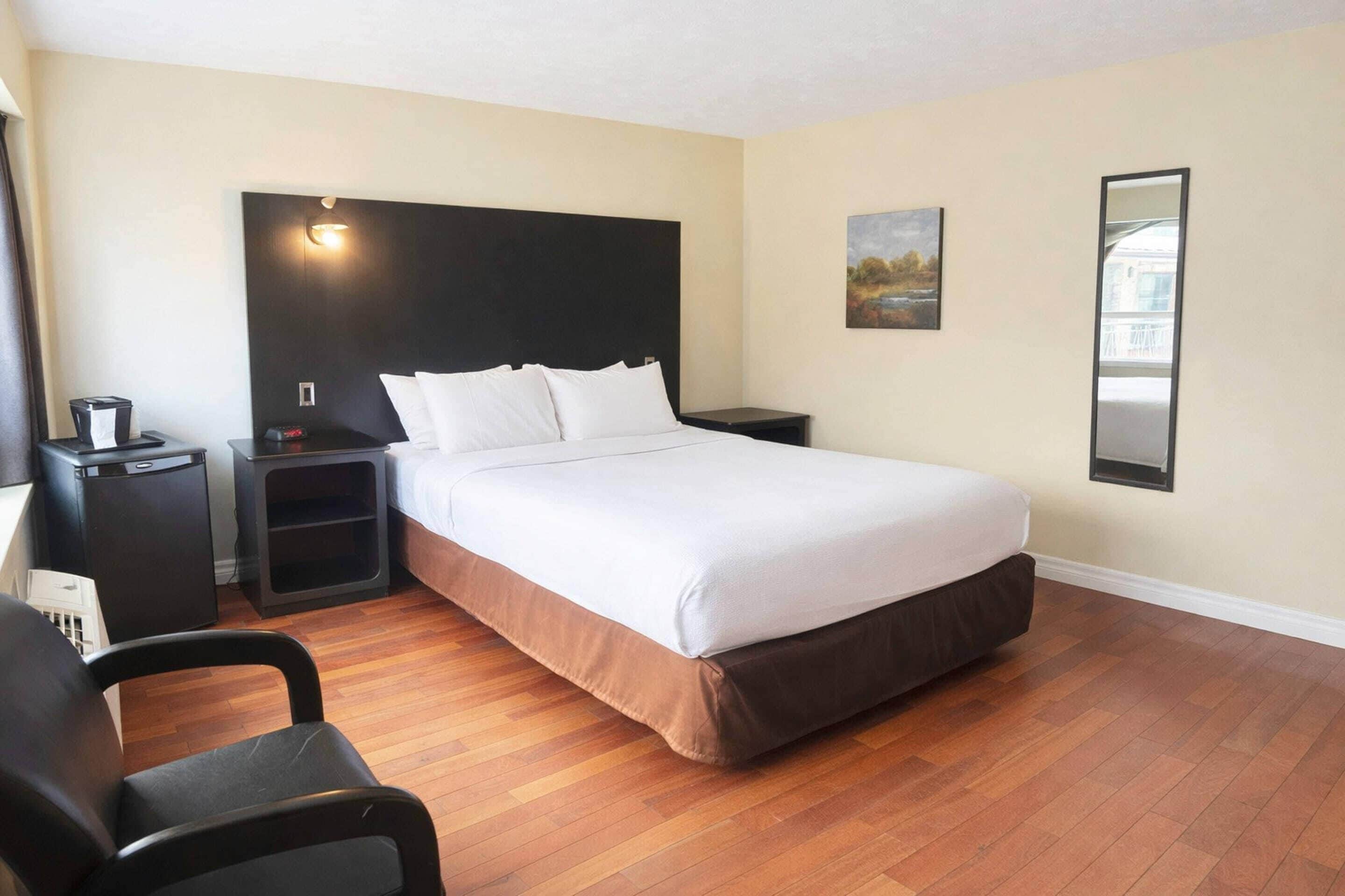 A hotel room with a large bed, bedside tables, a chair, and a painting on the wall.