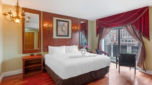 A hotel room with a large bed, a wooden nightstand, a mirror, a chandelier, a window with curtains, and a view of buildings outside. - Quality Hotel Fallsview Cascade (Niagara Falls)