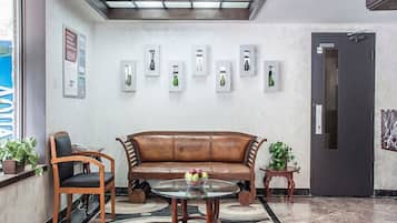 A lobby with a leather sofa, two chairs, a glass coffee table, and a patterned rug. There are framed pictures on the wall and a door labeled "ELEVATOR".