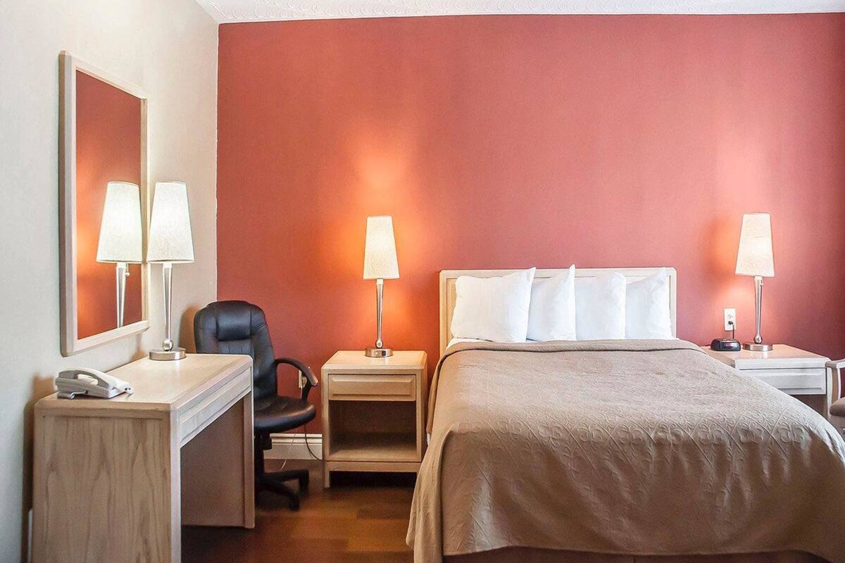 A hotel room with a bed, bedside lamps, a desk with a telephone, and a chair.