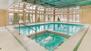 An indoor swimming pool with clear glass walls, a tiled floor, and a metal roof structure. - Quality Hotel Fallsview Cascade (Niagara Falls)